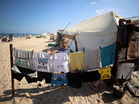 A displaced Palestinian girl hangs clothes outside her displaced family's tent at a makeshift camp on the beach of Deir al-Balah, central Ga...