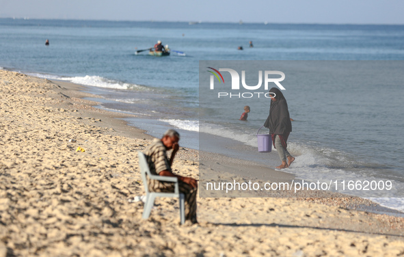 A displaced Palestinian transports a bucket of sea water on the beach of Deir al-Balah in the central Gaza Strip on October 13, 2024, amid t...