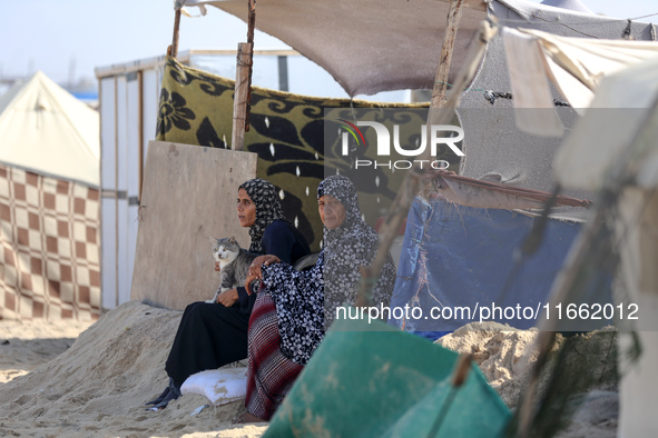 Displaced Palestinians sit outside their tent at a makeshift camp on the beach of Deir al-Balah in the central Gaza Strip on October 13, 202...