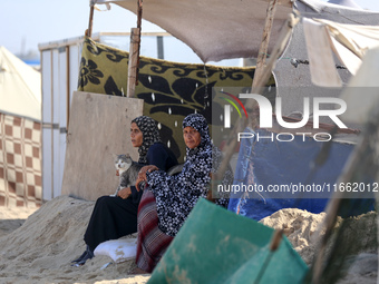 Displaced Palestinians sit outside their tent at a makeshift camp on the beach of Deir al-Balah in the central Gaza Strip on October 13, 202...