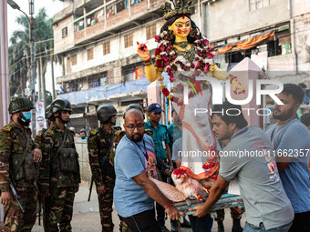 Bangladesh Army officers stand nearby to secure the area as Bangladeshi Hindu devotees immerse an idol of their deity Durga into the Burigan...