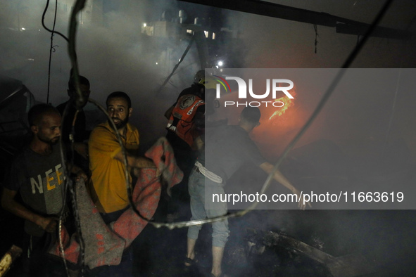 People attempt to extinguish a fire at the site of an Israeli strike on tents sheltering displaced people amid the Israel-Hamas conflict in...