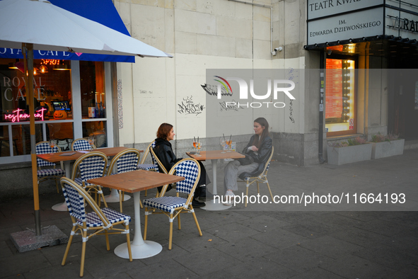 Two young woman are seen having drinks sitting outdoors at a cafe in Warsaw, Poland on 12 October, 2024. 