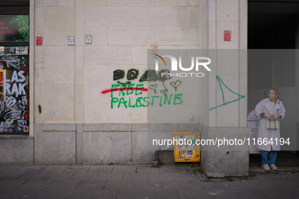 Grafitti reading "Palestine" is seen on a wall while a woman looks on in central Warsaw, Poland on 12 October, 2024. 