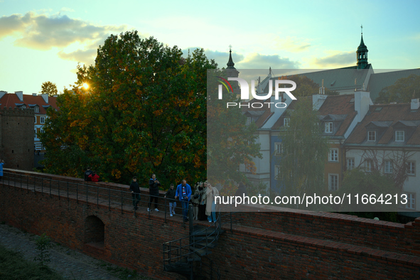 People are seen taking selfies on the Old Town city wall while the sun sets in Warsaw, Poland on 12 October, 2024. 