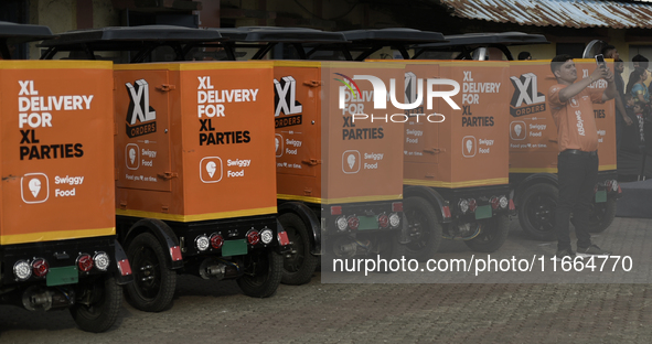 A Swiggy gig worker clicks a mobile selfie picture in front of an electric three-wheeler during a promotional event in Mumbai, India, on Oct...