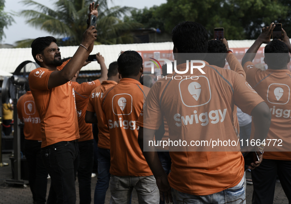 A Swiggy gig worker clicks a mobile selfie picture in front of an electric three-wheeler during a promotional event in Mumbai, India, on Oct...