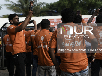 A Swiggy gig worker clicks a mobile selfie picture in front of an electric three-wheeler during a promotional event in Mumbai, India, on Oct...