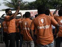 A Swiggy gig worker clicks a mobile selfie picture in front of an electric three-wheeler during a promotional event in Mumbai, India, on Oct...