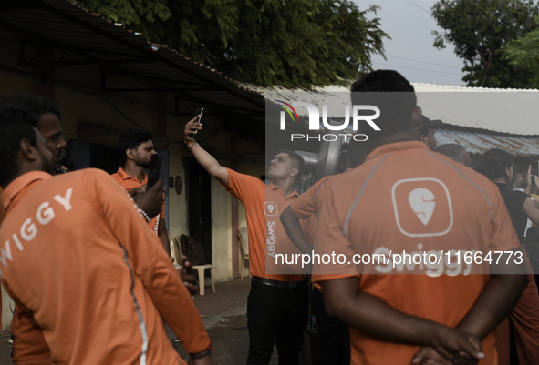 A Swiggy gig worker clicks a mobile selfie picture in front of an electric three-wheeler during a promotional event in Mumbai, India, on Oct...