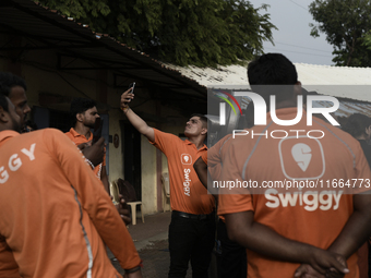 A Swiggy gig worker clicks a mobile selfie picture in front of an electric three-wheeler during a promotional event in Mumbai, India, on Oct...