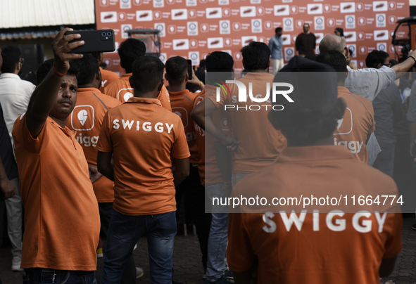 A Swiggy gig worker clicks a mobile selfie picture in front of an electric three-wheeler during a promotional event in Mumbai, India, on Oct...