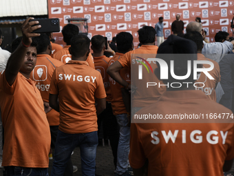 A Swiggy gig worker clicks a mobile selfie picture in front of an electric three-wheeler during a promotional event in Mumbai, India, on Oct...