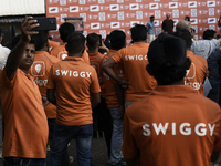 A Swiggy gig worker clicks a mobile selfie picture in front of an electric three-wheeler during a promotional event in Mumbai, India, on Oct...