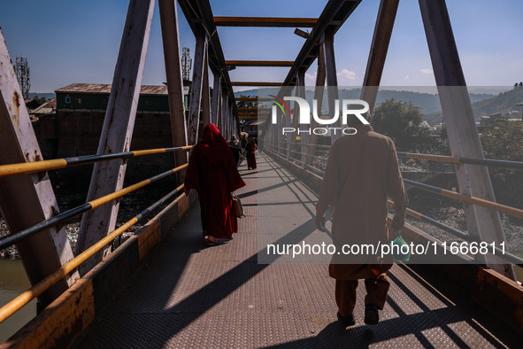 People walk on a pedestrian iron bridge on a sunny day in Baramulla, Jammu and Kashmir, India, on October 15, 2024. 