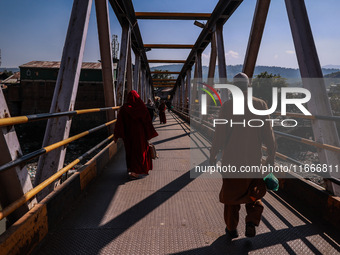 People walk on a pedestrian iron bridge on a sunny day in Baramulla, Jammu and Kashmir, India, on October 15, 2024. (