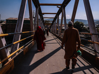 People walk on a pedestrian iron bridge on a sunny day in Baramulla, Jammu and Kashmir, India, on October 15, 2024. (