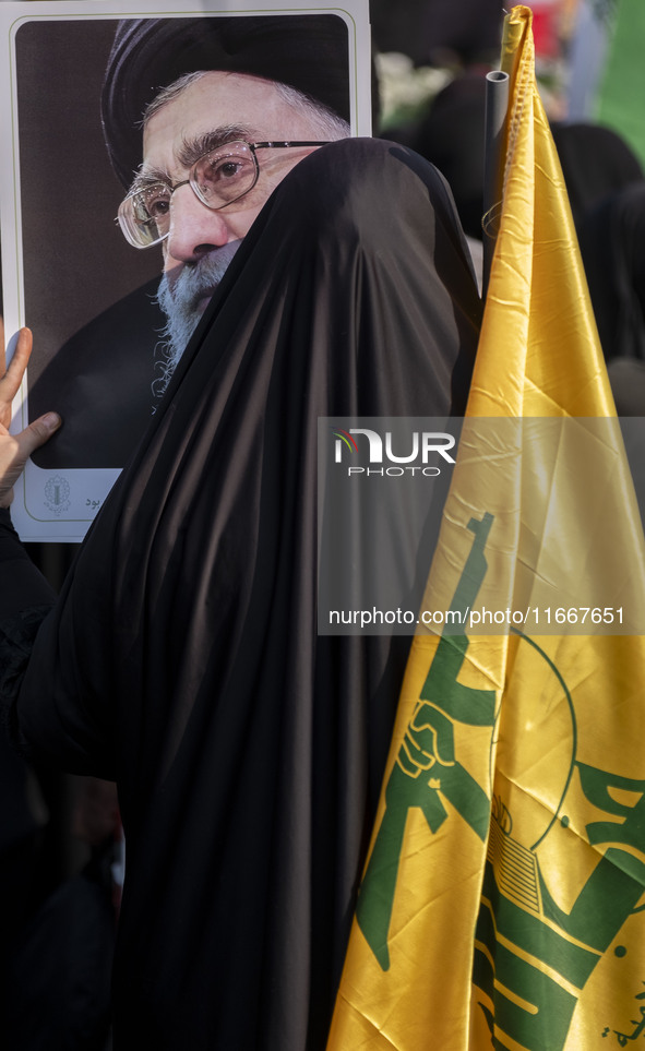 A veiled Iranian woman holds a portrait of Iran's Supreme Leader, Ayatollah Ali Khamenei, and a flag of Lebanon's Hezbollah while taking par...