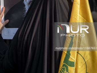 A veiled Iranian woman holds a portrait of Iran's Supreme Leader, Ayatollah Ali Khamenei, and a flag of Lebanon's Hezbollah while taking par...