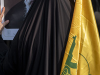 A veiled Iranian woman holds a portrait of Iran's Supreme Leader, Ayatollah Ali Khamenei, and a flag of Lebanon's Hezbollah while taking par...