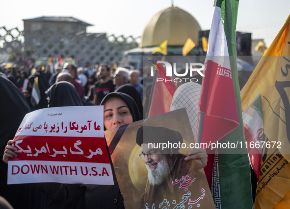 A veiled Iranian mourner holds a portrait of Lebanon's Hezbollah late leader, Hassan Nasrallah, and an anti-U.S. placard while taking part i...