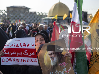 A veiled Iranian mourner holds a portrait of Lebanon's Hezbollah late leader, Hassan Nasrallah, and an anti-U.S. placard while taking part i...