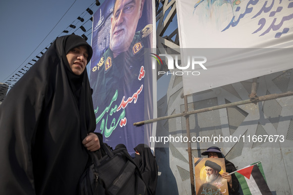 A veiled Iranian mourner holds a Palestinian flag and a portrait of Lebanon's Hezbollah leader, Hassan Nasrallah, while a veiled woman walks...