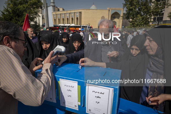 Iranian mourners place bank receipts into charity boxes meant to help the people of Lebanon, Gaza, and Yemen after participating in the fune...