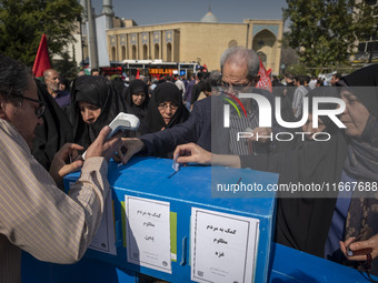 Iranian mourners place bank receipts into charity boxes meant to help the people of Lebanon, Gaza, and Yemen after participating in the fune...