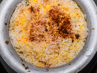 A pot of biryani, with aromatic basmati rice, cooked chicken, and a variety of spices such as saffron, kewra water, and fried onions known a...