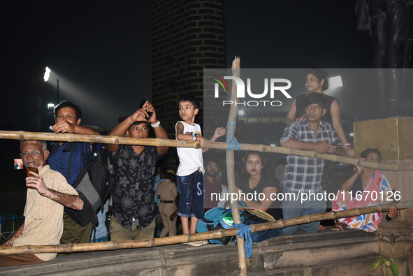 People stand and watch a street-side barricade in a procession with Durga idols before the immersion of the statue of Goddess Durga into the...