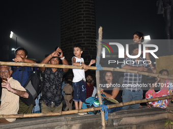 People stand and watch a street-side barricade in a procession with Durga idols before the immersion of the statue of Goddess Durga into the...