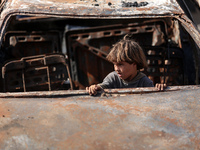 A displaced Palestinian boy looks out from a destroyed car due to an Israeli airstrike on the tents of the displaced inside the Al-Aqsa Mart...