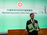 Hong Kong Chief Executive John Lee holds up booklets of his 2024 policy address while posing for a photo before a press conference in Hong K...