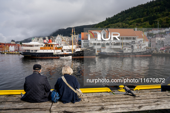 Tourists sit on a bench overlooking the harbor of Bergen, Norway, on September 16, 2024. Bergen is the second-largest city in Norway, with a...