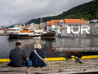 Tourists sit on a bench overlooking the harbor of Bergen, Norway, on September 16, 2024. Bergen is the second-largest city in Norway, with a...