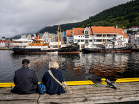 Tourists sit on a bench overlooking the harbor of Bergen, Norway, on September 16, 2024. Bergen is the second-largest city in Norway, with a...