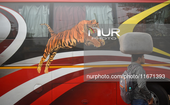 A person carries a sack on his head while walking next to a bus inside a bus stand in Kolkata, India, on October 16, 2024. 