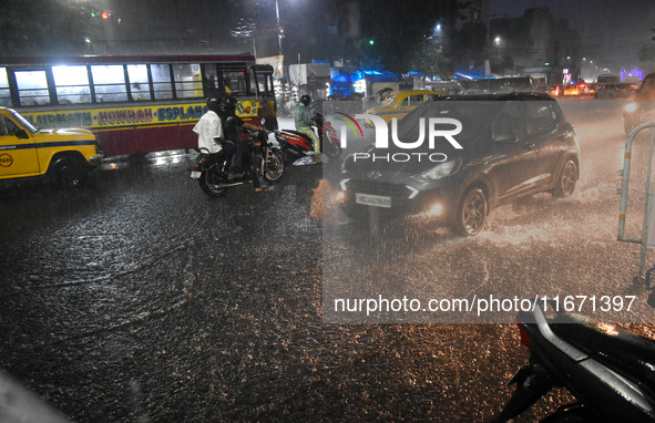 People stand at a traffic signal during heavy rain in Kolkata, India, on October 16, 2024. 