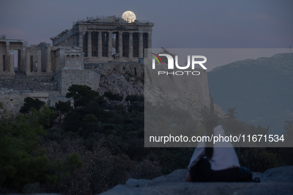 A tourist watches the October 'Hunter's supermoon' rise above the Greek Parthenon Temple (438 BC), covered by scaffolding, at the Acropolis...