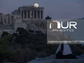 A tourist watches the October 'Hunter's supermoon' rise above the Greek Parthenon Temple (438 BC), covered by scaffolding, at the Acropolis...