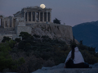 A tourist watches the October 'Hunter's supermoon' rise above the Greek Parthenon Temple (438 BC), covered by scaffolding, at the Acropolis...