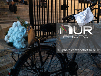 This photograph shows a bicycle carrying a bunch of white flowers and bearing a message that reads ''Stop to road violence! Victims: bike us...