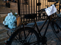 This photograph shows a bicycle carrying a bunch of white flowers and bearing a message that reads ''Stop to road violence! Victims: bike us...