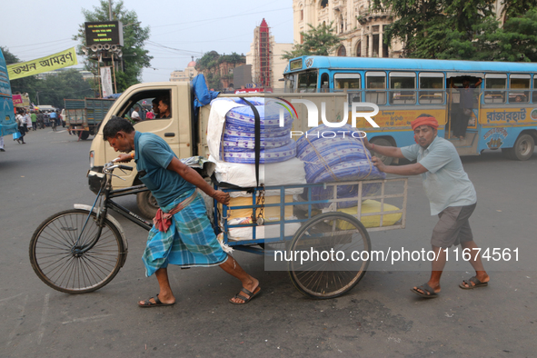 Indian laborers push a cycle van loaded with goods across a busy road in Kolkata, India, on October 17, 2024. 