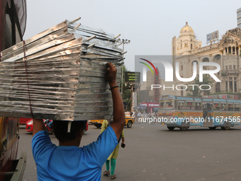 Indian daily laborers carry goods and cross a busy road in Kolkata, India, on October 17, 2024. (