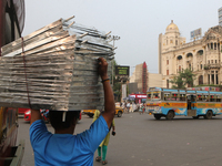 Indian daily laborers carry goods and cross a busy road in Kolkata, India, on October 17, 2024. (