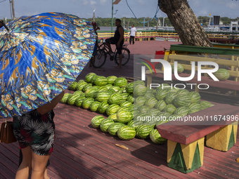 A woman with umbrellas looks at melons in the town's port in Afua, Para, Brazil, on September 29, 2024. (