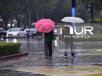 People wear thick clothes and walk in the rain in Qingzhou, China, on October 18, 2024. (