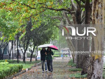 People wear thick clothes and walk in the rain in Qingzhou, China, on October 18, 2024. (